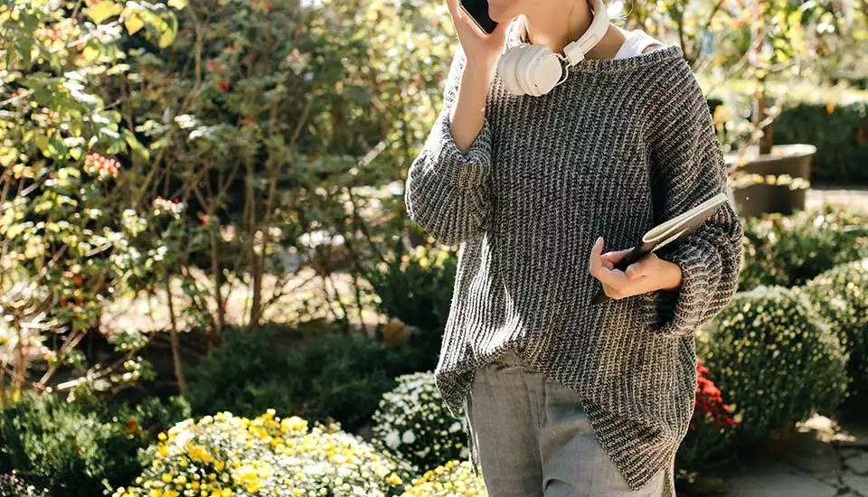 kvinna går med telefon och block under armen i en trädgård