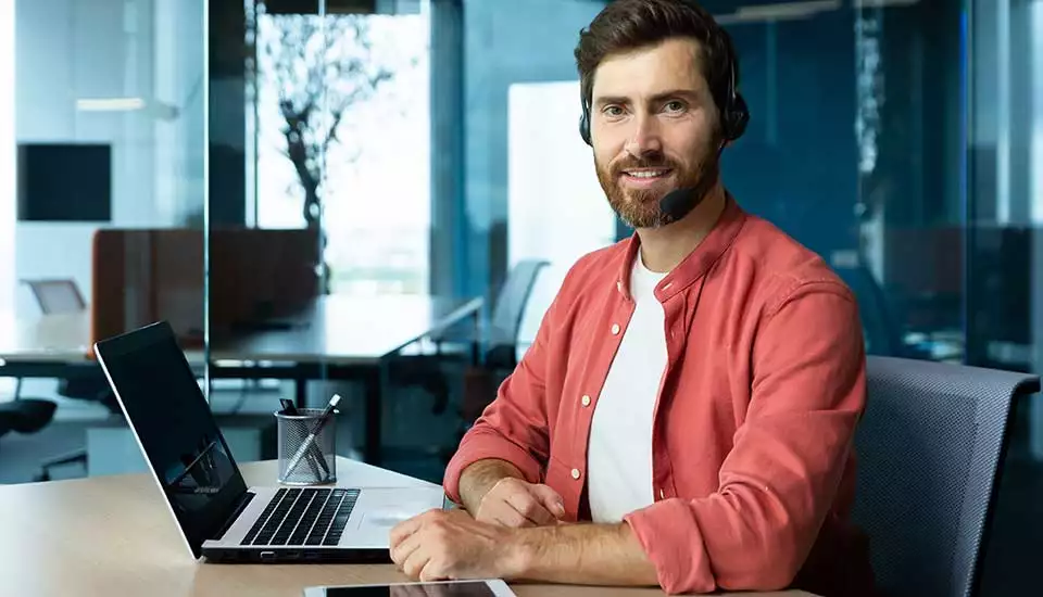 man i röd skjorta sitter framför laptop vid skrivbord