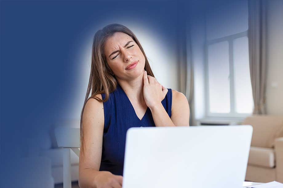 Kvinna sitter framför datorn och tar sig om nacken och har ont