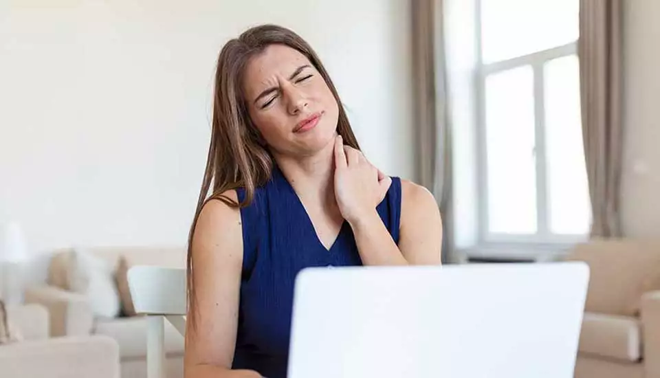 Kvinna sitter framför datorn och tar sig om nacken och har ont