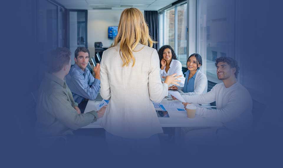Teambuildingaktivitet där en person leder en engagerad grupp i samtal runt ett bord i en modern kontorsmiljö.